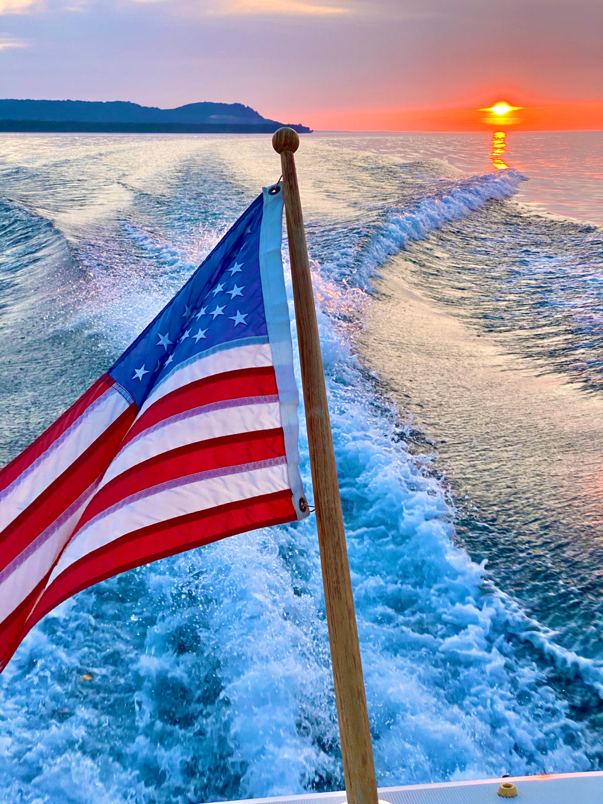 An American flag at the back of a moving boat, with a beautiful sunset in the background.
