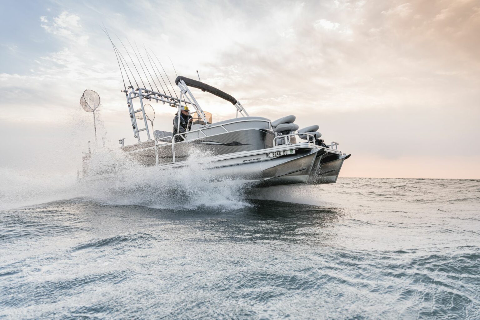 Royalty-free image - A motorboat speeds across the water, creating a spray against a backdrop of a cloudy sky. The boat is equipped with fishing rods and other gear, suggesting it is used for fishing activities.