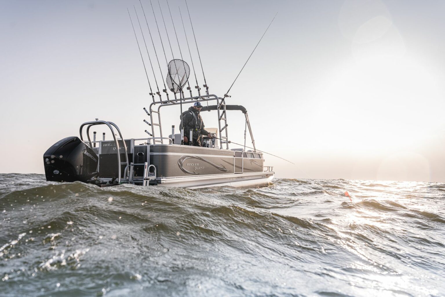 Royalty-free image - A fishing boat with multiple rods and a net on board is navigating through slightly choppy waters under a bright, clear sky. Sunlight reflects off the water, creating a serene, early morning scene.