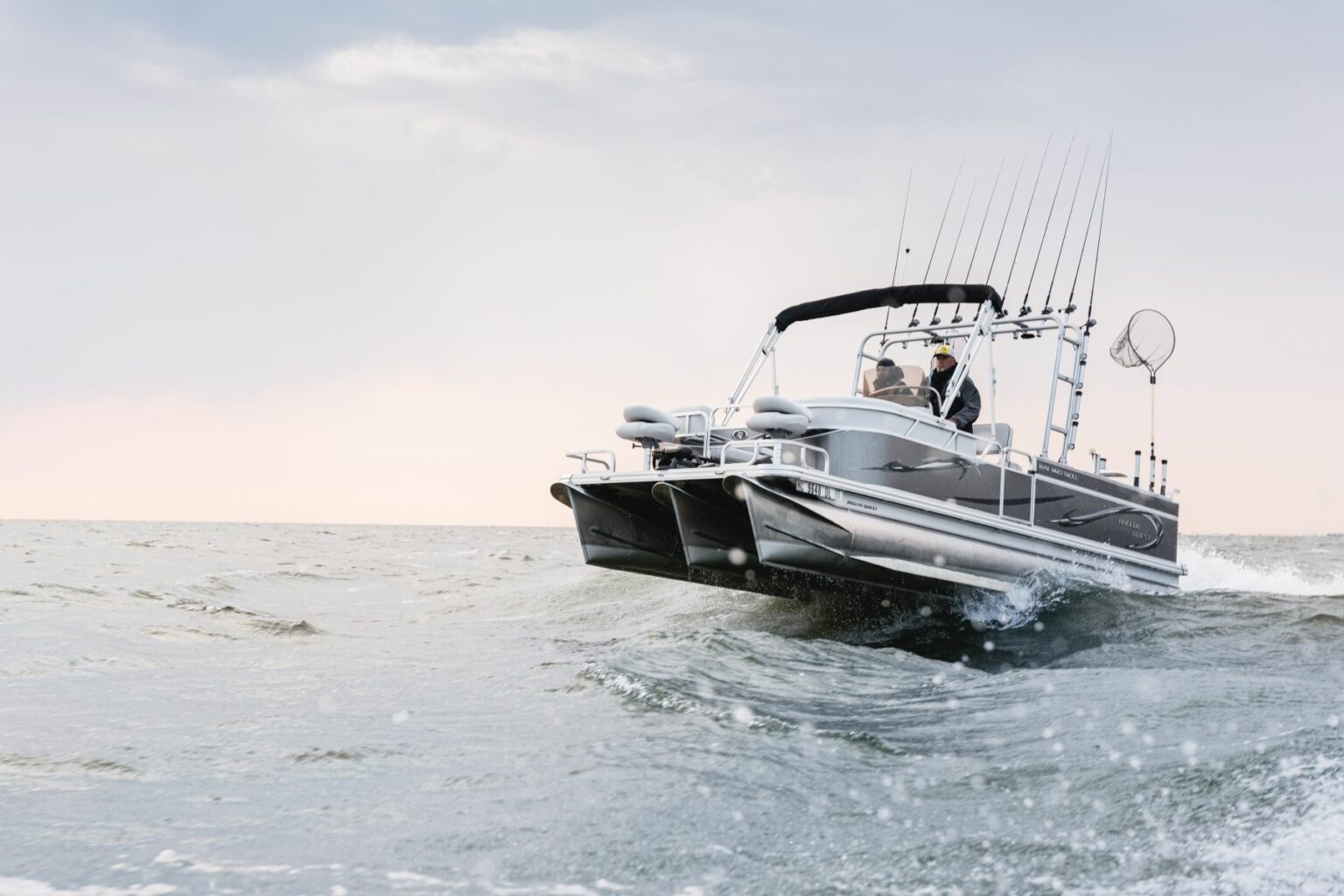 Royalty-free image - A motorized fishing boat with multiple fishing rods moves quickly through the ocean, creating splashes. The sky is overcast, and the horizon is visible in the background.