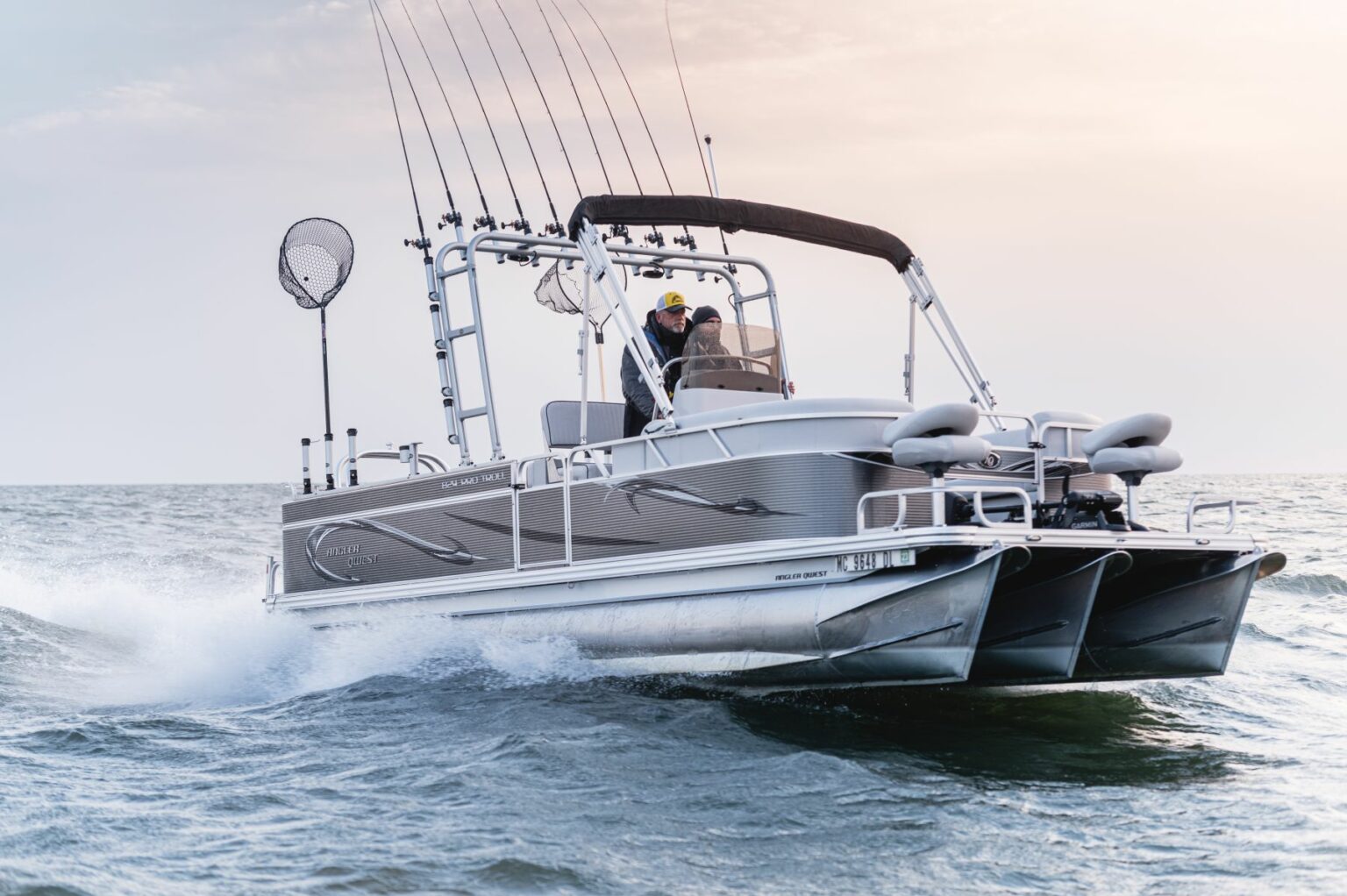 Royalty-free image - A sleek motorboat cruises through the ocean with fishing gear visible on board. The hull is silver, and the water splashes around the boat, indicating speed. The sky is a soft gradient, suggesting early morning or late afternoon.