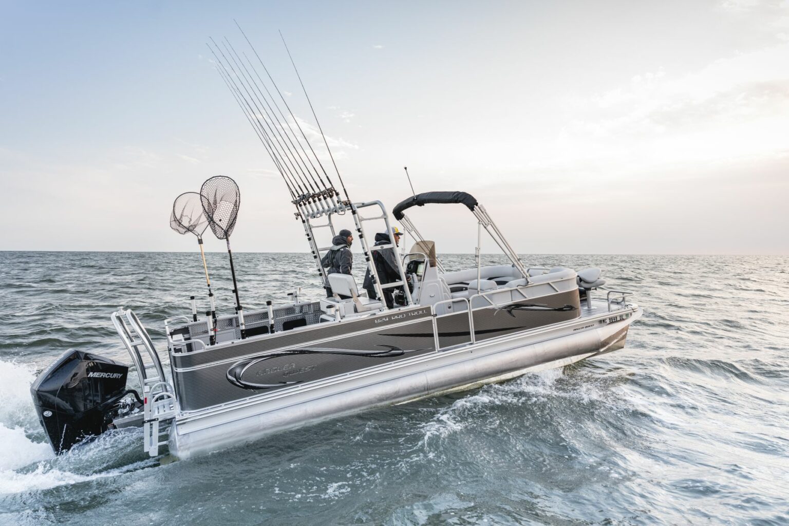 Royalty-free image - A fishing boat with multiple fishing rods and nets is moving through the water. Two people are seated on the boat beneath a clear sky. The boat is equipped with a Mercury motor. The waves around the boat indicate movement.