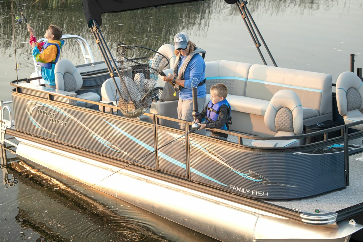 Royalty-free image - A family on a pontoon boat is fishing. An adult holds a net with a fish in it, while two children stand nearby, one holding a fishing rod. The boat is on calm water, and they are all wearing life jackets.