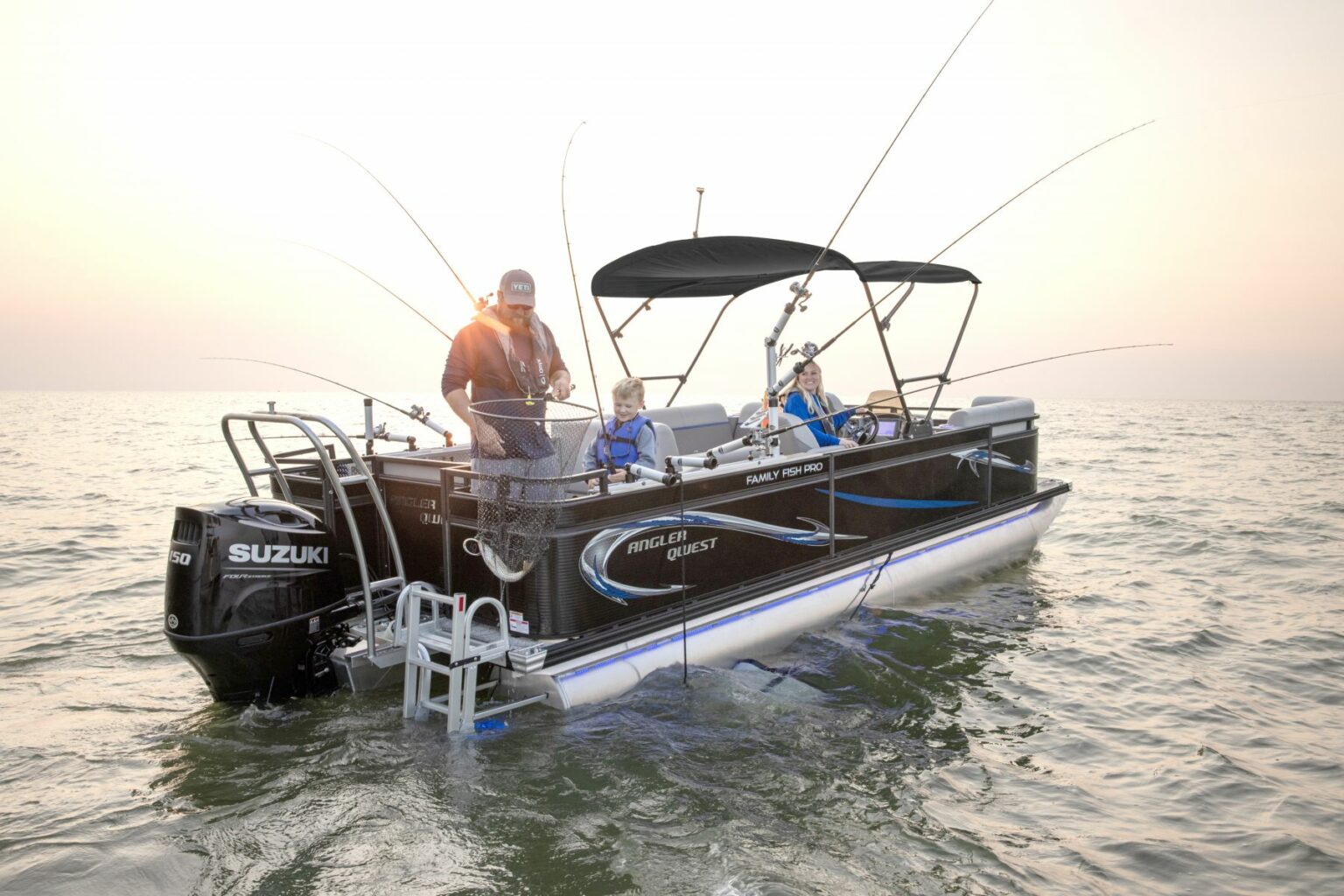 License-free image A family of three, including a man, a woman, and a child, are fishing on a pontoon boat equipped with several fishing rods. The boat is floating on calm water, and the sun is setting in the background, casting a warm glow over the scene.