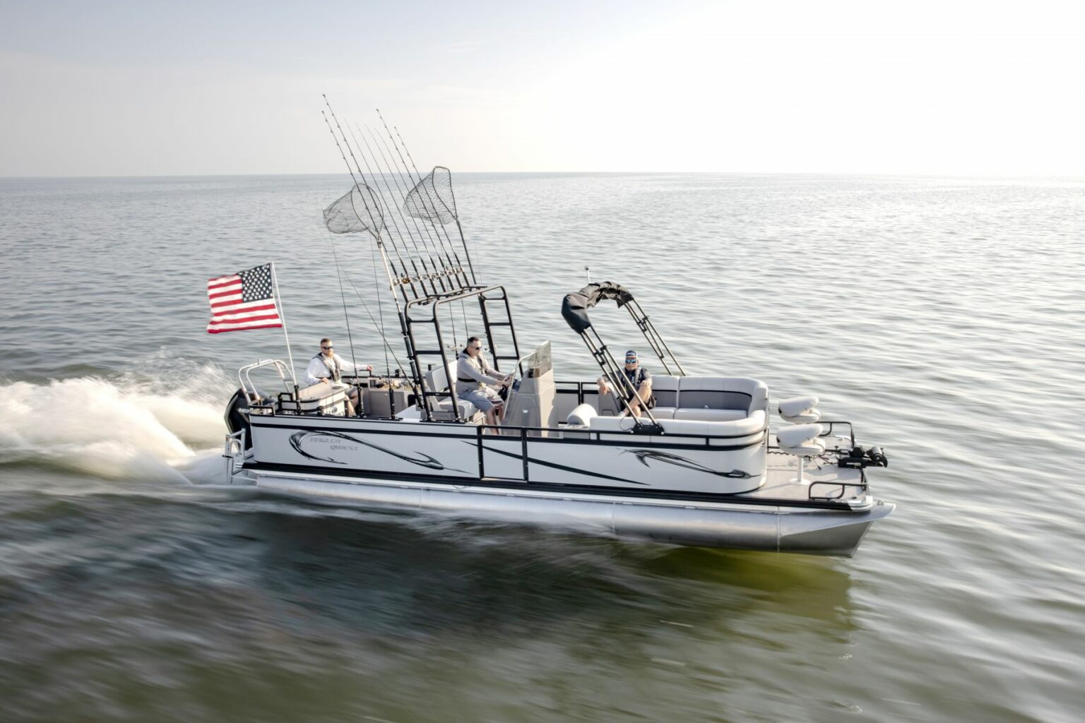 Royalty-free image - A motorized fishing boat glides across calm waters with an American flag at the stern. Four passengers are on board, and several fishing rods are mounted at the back. The sky is clear, and the water reflects the light.