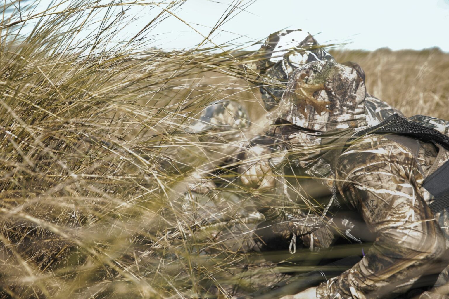 Royalty-free image - Camouflaged soldiers crouch in tall grass, blending into the natural surroundings. They wear uniforms with earthy patterns, emphasizing stealth in the outdoor environment. Hunting from a jon boat in the marsh along the St. Johns River near Christmas, Florida.