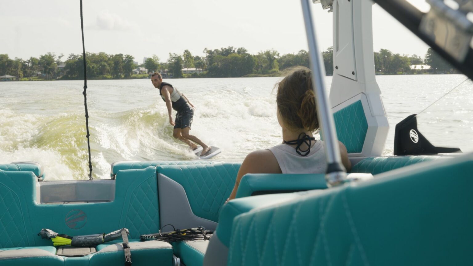 License-free image - Wake surfer riding the wake behind a wake boat. Passenger in boat spotting the wake surfer for the driver