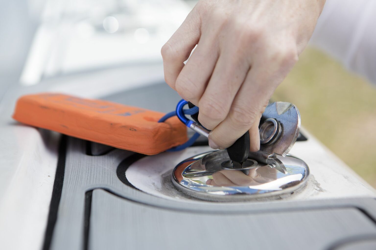 License-free image - A person&#039;s hand turning a metal key in a boat ignition with an attached orange float. Opening a locked gas cap on a boat.