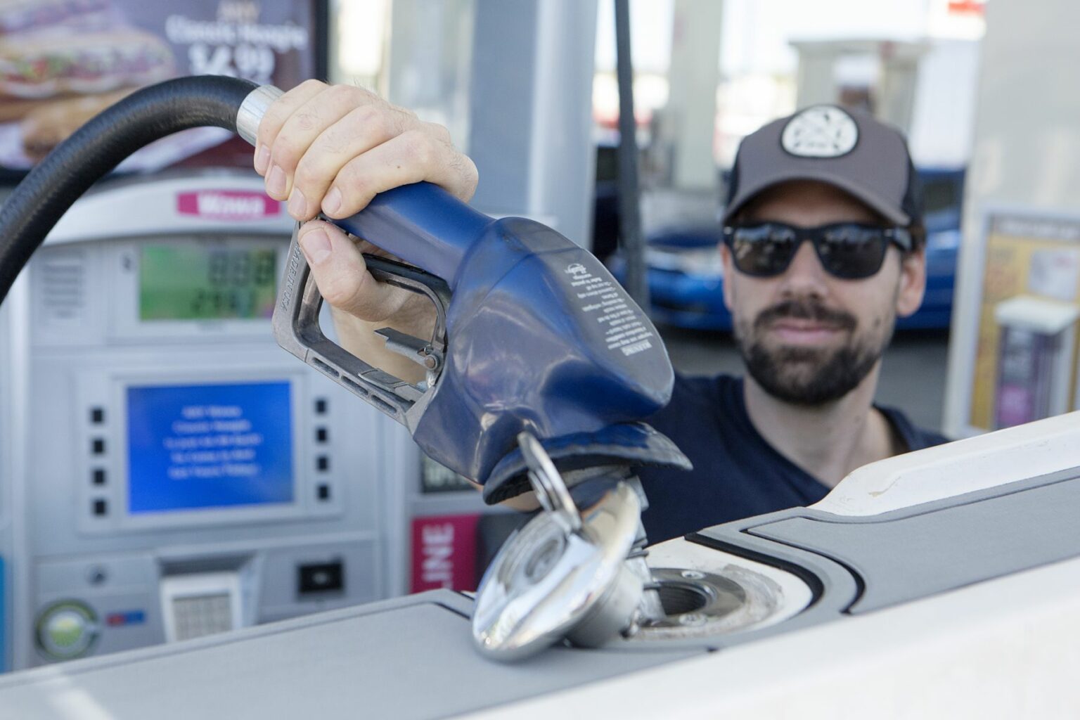 License-free image - A man wearing a cap and sunglasses is pumping gas into a vehicle at a gas station. He holds the fuel nozzle with one hand, and the fuel pump and price per gallon display can be seen in the background. Refueling a boat at a land pump.