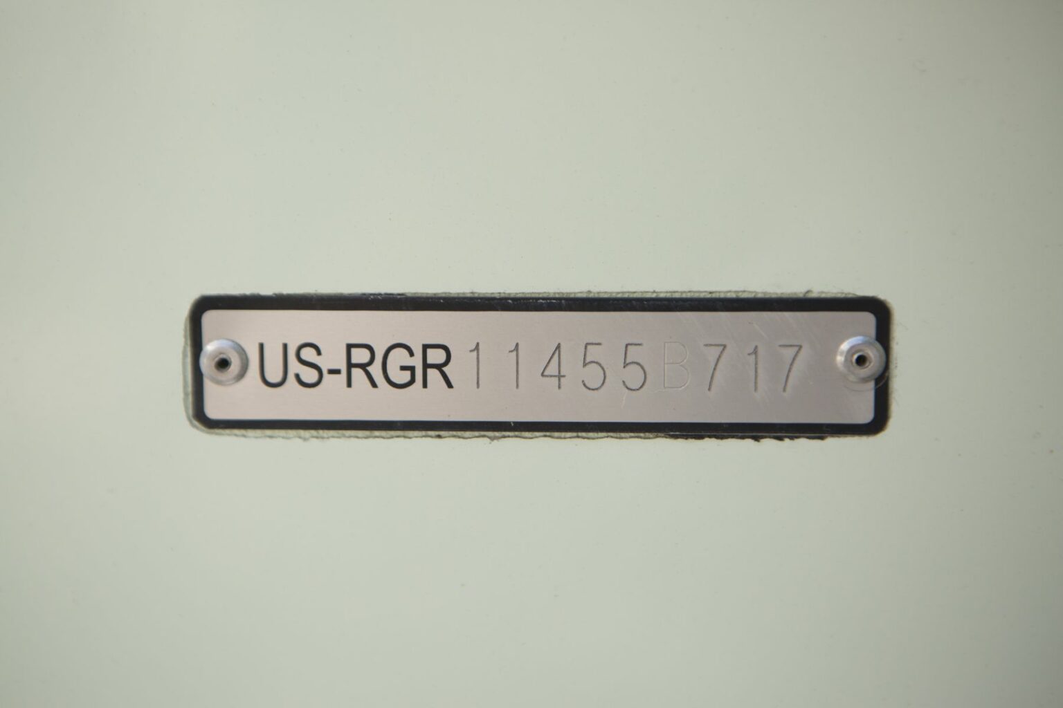 License-free image - A close-up of a metallic label plate with the engraving &quot;US-RGR 11455B717&quot; secured by two screws on a light-colored surface. A hull identification number on a watercraft.