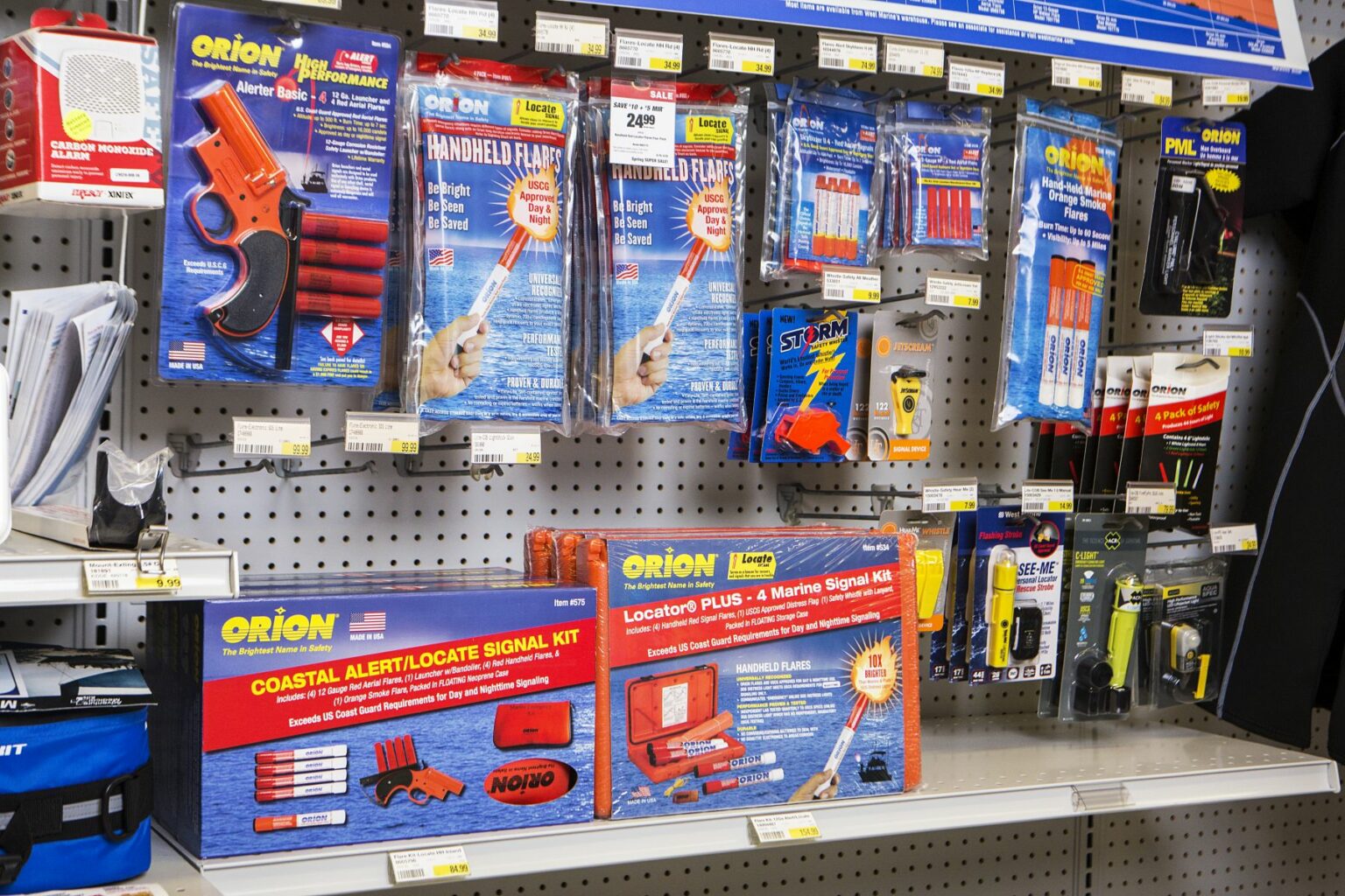 License-free image - A store shelf displaying various marine safety and signaling devices, including flare guns, flare packs, signal kits, and electronic distress signals. The products are from brands like Orion and are neatly arranged in their respective packaging. Flares and other safety equipment on the shelves at a retail outlet.