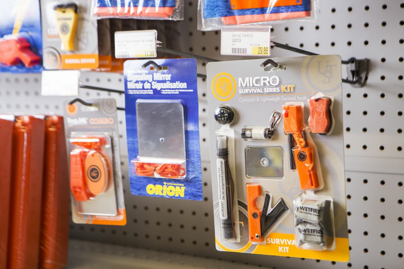 License-free image -  A retail display features various survival kits and tools hanging on hooks. Items include a micro survival series kit, an emergency signaling mirror, and a signal device. Packaging displays vibrant orange and blue colors, with clearly labeled prices and barcodes. Signaling mirrors and other safety equipment on the shelves at a retail outlet.