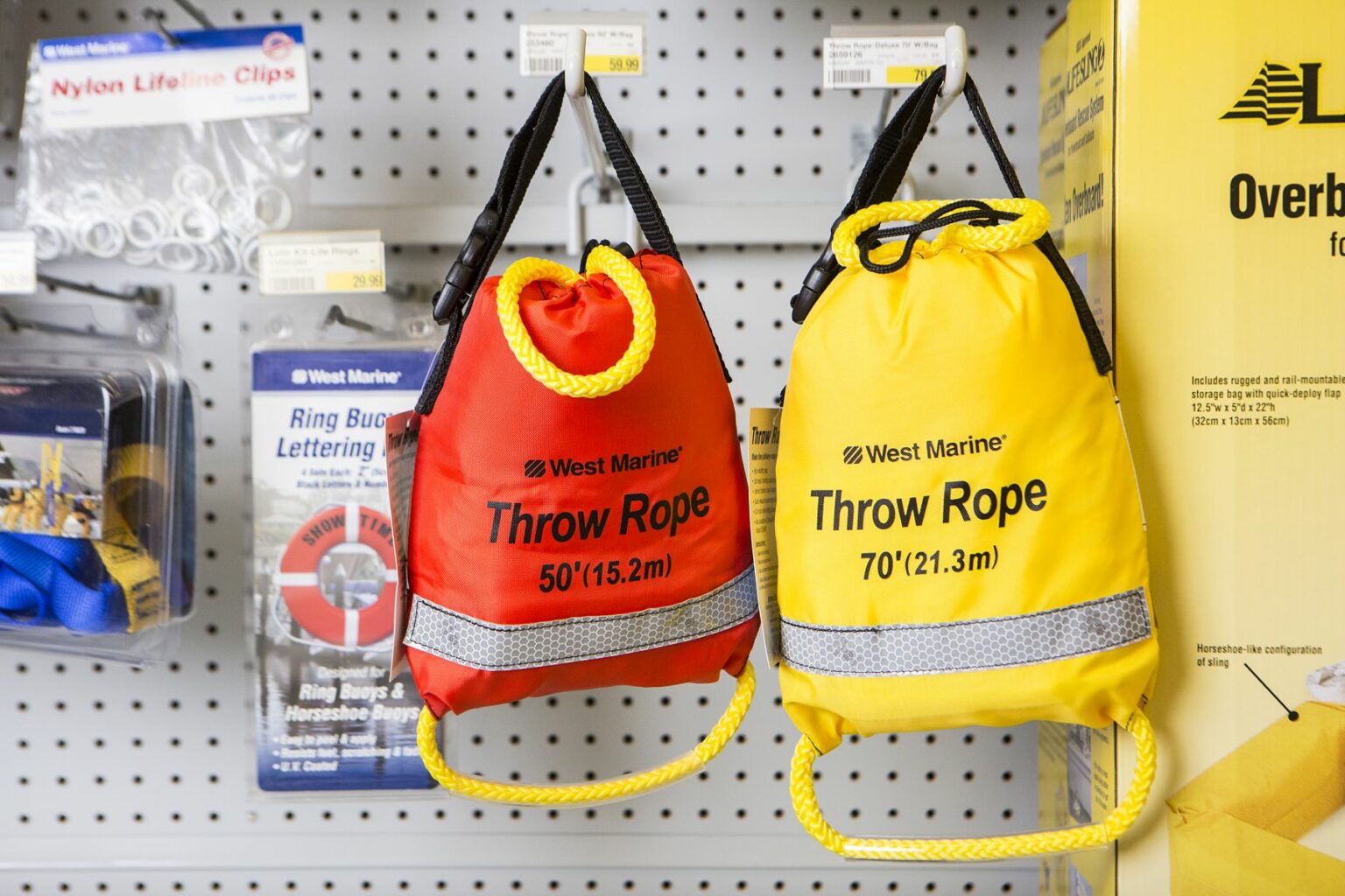 License-free image - Two throw rope bags hanging on display in a store. The red bag has a 50 feet (15.2 meters) rope, and the yellow bag has a 70 feet (21.3 meters) rope. Both bags have black straps and reflective bands. Other boating accessories are visible in the background. Safety equipment on display at a retail outlet.