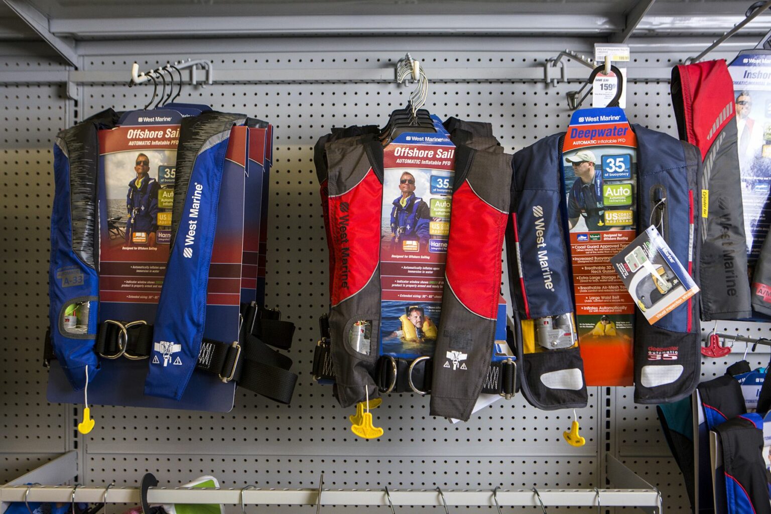 License-free image - Three different models of life jackets are displayed on a store rack. The jackets are packaged in plastic and feature various designs and colors, including blue and red. Each package contains product information and images of people wearing the life jackets. Safety equipment on display at a retail outlet.