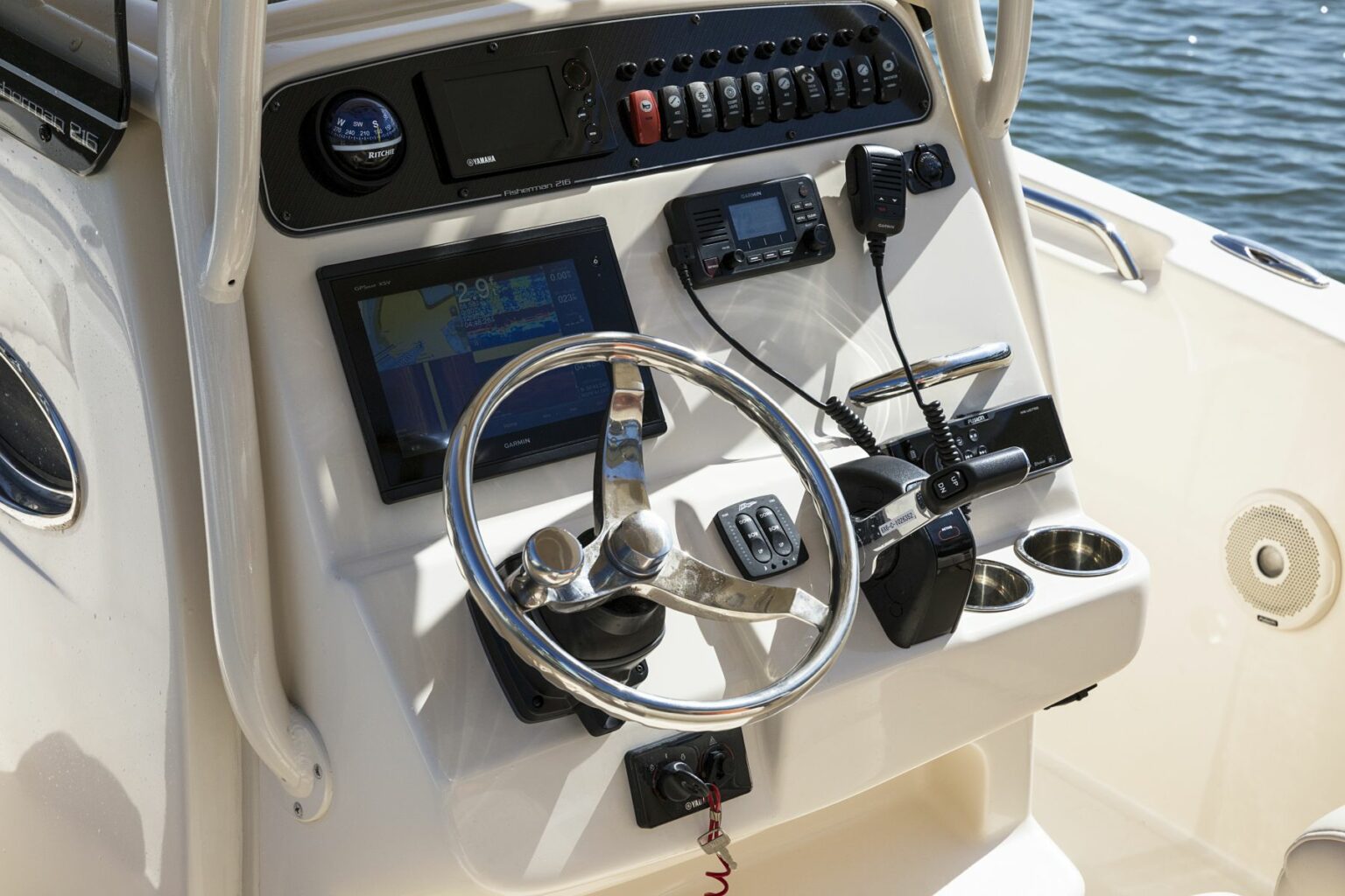 License-free image - Close-up of a boat&#039;s control console with a steering wheel, various navigational instruments, buttons, and communication devices. A screen displays a digital navigation map. The console has cup holders and is set against a backdrop of water. Using GPS aboard a vessel in Bath, North Carolina.