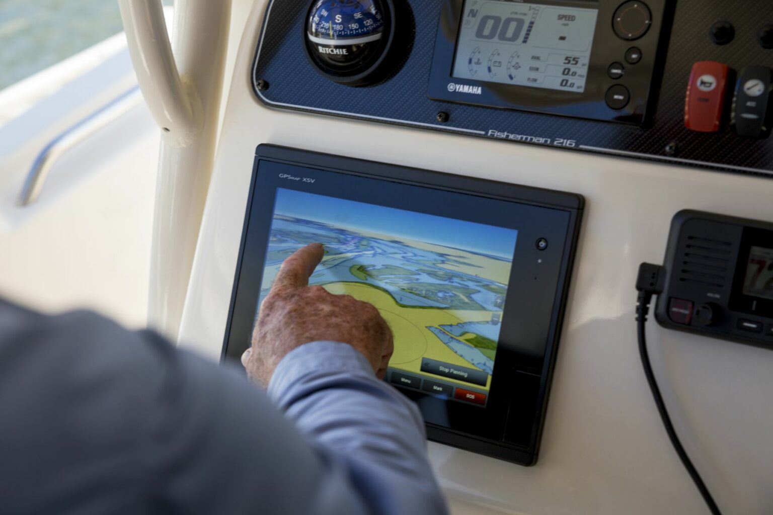 License-free image A person interacts with a touchscreen navigation system on a boat&#039;s control panel. The screen displays a colorful map with various buttons, while other gauges and controls, like a speedometer and radio, are also visible nearby. The boat appears to be moving on water.