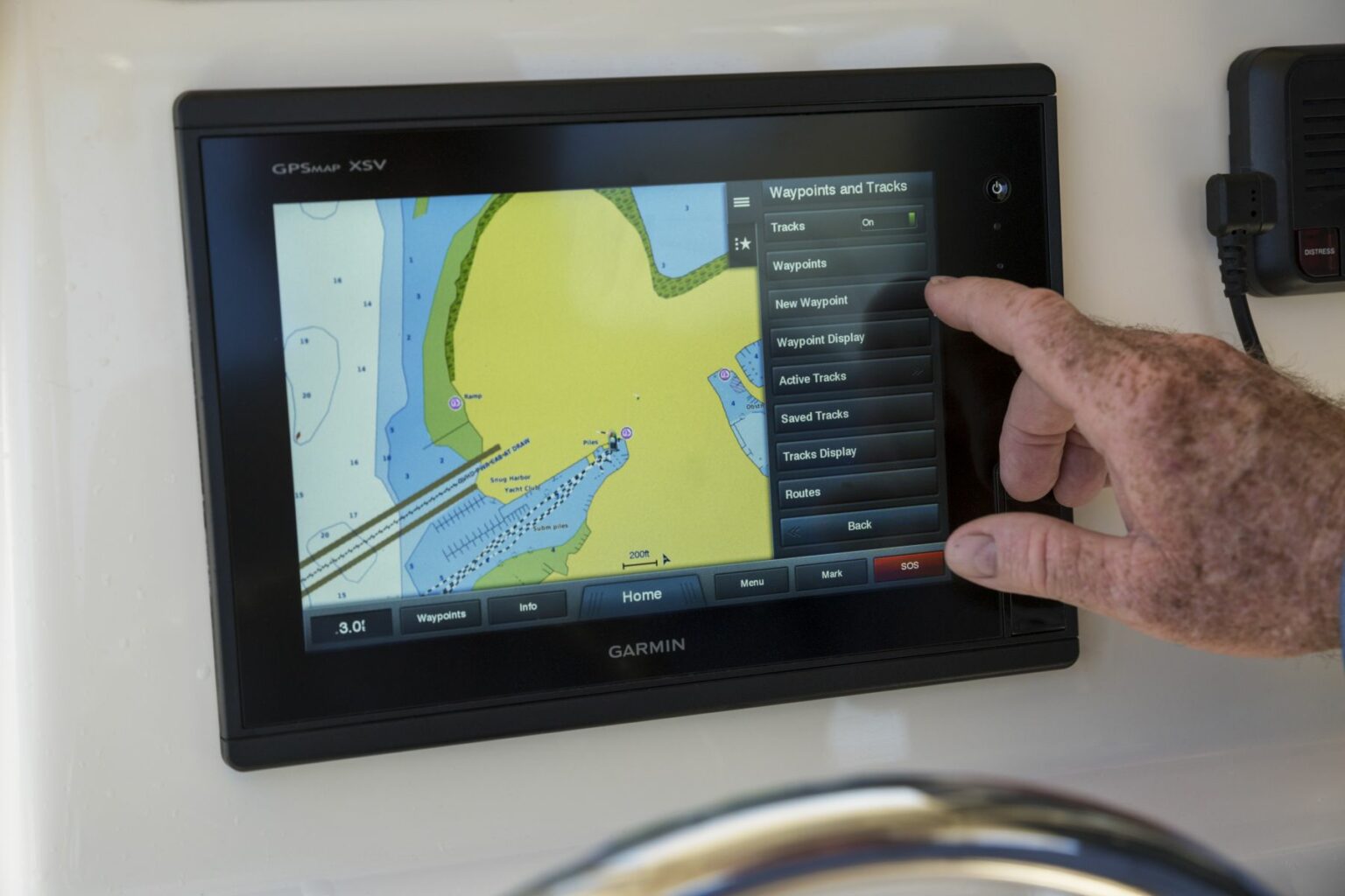 Royalty-free image - A person interacts with a Garmin GPSMap 7410xsv touchscreen, showing a nautical chart. The screen displays waypoints and tracks options. A hand is pointing at the &quot;Tracks&quot; section on the display. Using GPS aboard a vessel in Bath, North Carolina.