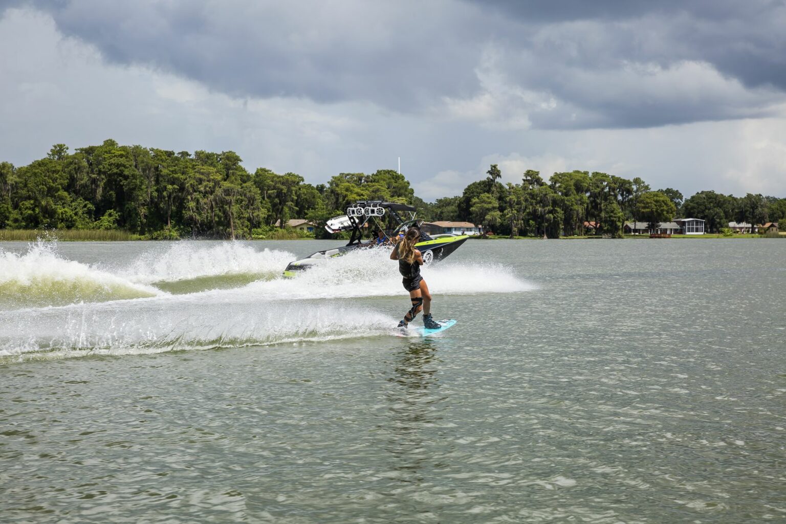 License-free image - A person wakeboarding on a lake is being pulled by a speedboat. The sky is cloudy, and the shoreline is visible in the background, lined with trees and a few buildings. Another speedboat is seen creating waves near the wakeboarder. Wakeboarding behind a wakeboard boat on Clear Lake in Orlando, Florida.