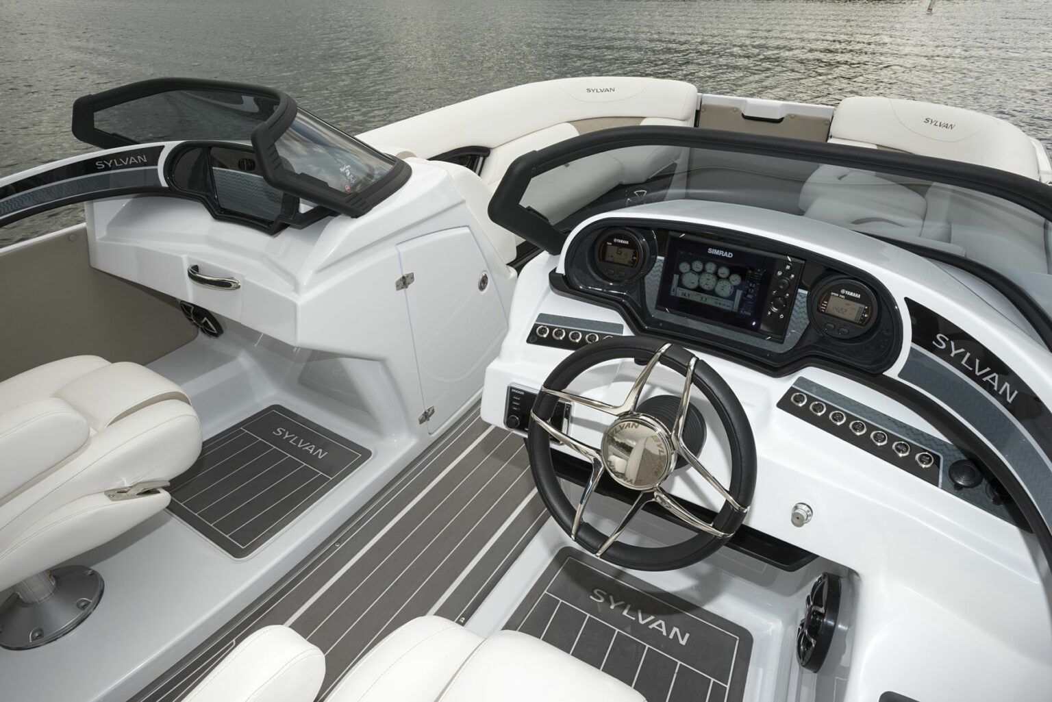 License-free image - A modern boat cockpit featuring a sleek steering wheel, multiple digital displays, and a comfortable seating area. The boat is at rest on the water. The interior is white with grey accents and the brand name &quot;Sylvan&quot; is visible on the dashboard and seats. A deck free of hazards.