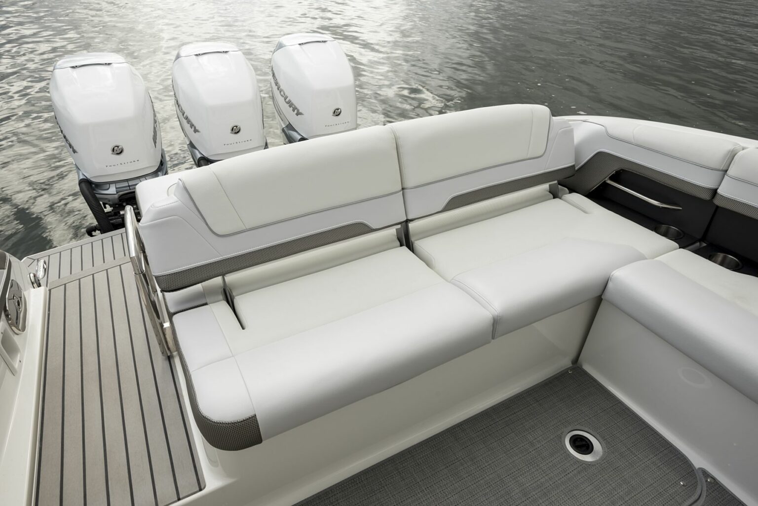 License-free image - The image shows the interior of the rear section of a boat, featuring white cushioned seating and three outboard motors on the stern. The boat is situated on calm water, and the floor has a grey, textured surface with wood-finish side panels. A deck free of hazards.