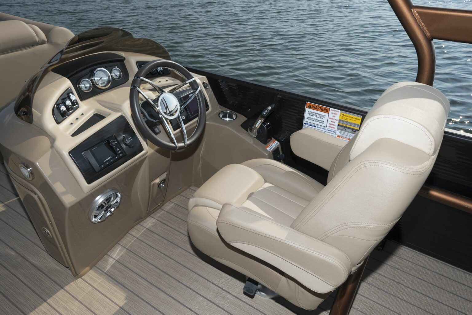 License-free image - Captain&#039;s chair and steering console of a boat with beige cushioned seat, steering wheel, and various control panels. The background shows water, and there are safety instructions posted on the right side of the console. The deck is wooden. A capacity plate and certificate of compliance.