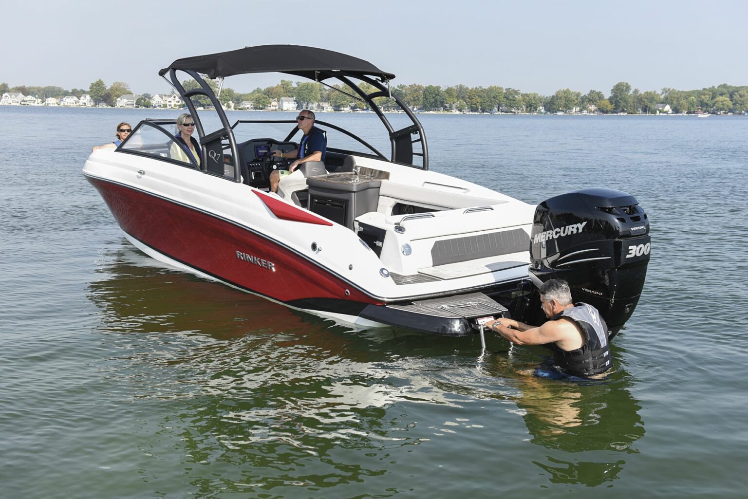 License-free image - A sleek, red and white powerboat with a black canopy is floating on calm waters. Three people are visible: one man in the water at the back of the boat, and two individuals seated on the boat. The outboard motor reads &quot;300 MERCURY.&quot; Trees are in the background.