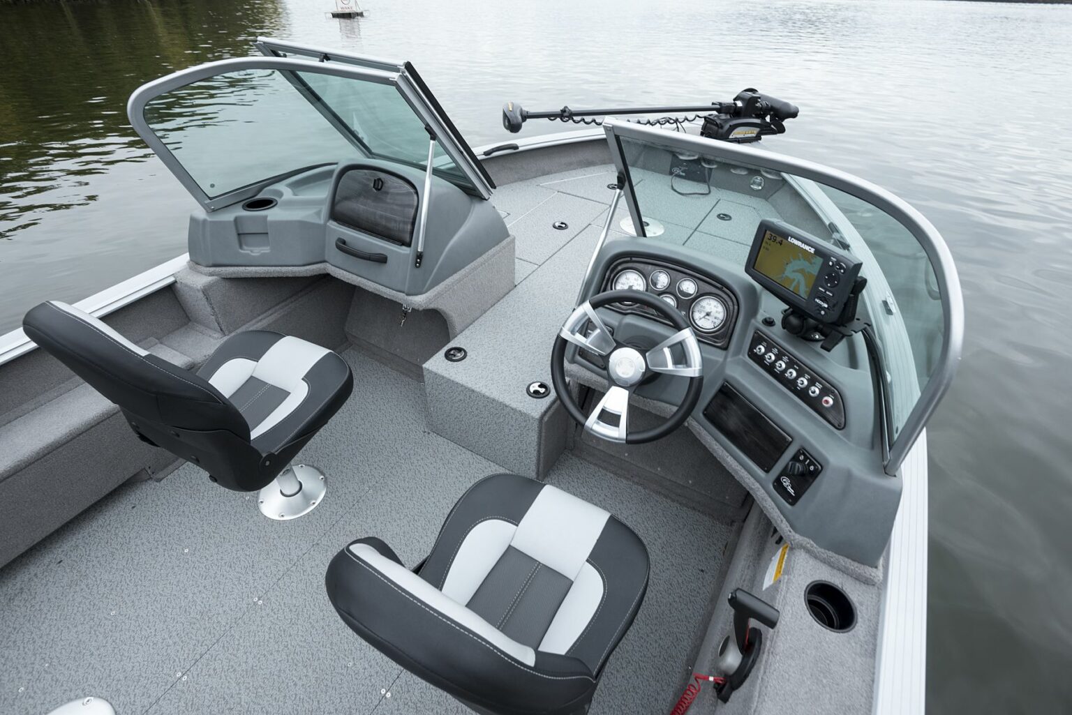 License-free image - Interior view of a modern fishing boat with two seats, steering wheel, electronic display for navigation, and fishing rod holder. The boat is on calm water, surrounded by greenery. The overall design appears functional and suited for fishing activities. A deck free of hazards.