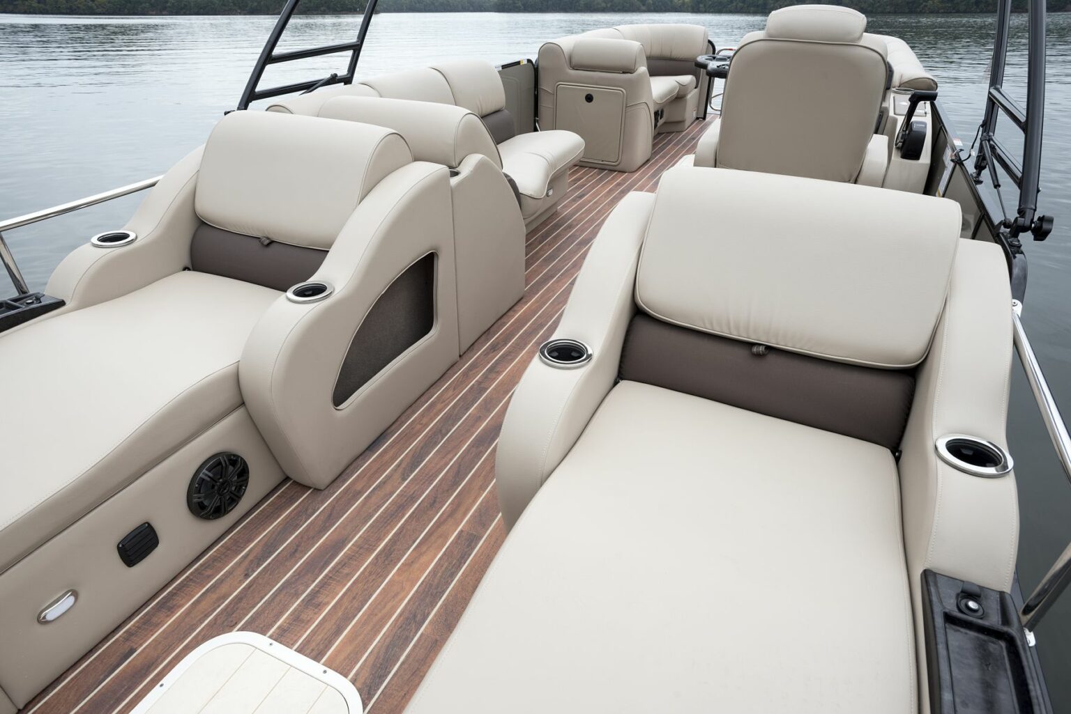 License-free image - The image shows a luxurious boat deck featuring comfortable, tan leather, cushioned seating with cup holders, set on a polished wooden floor. The boat is on calm water, with some greenery visible in the background. A deck free of hazards.