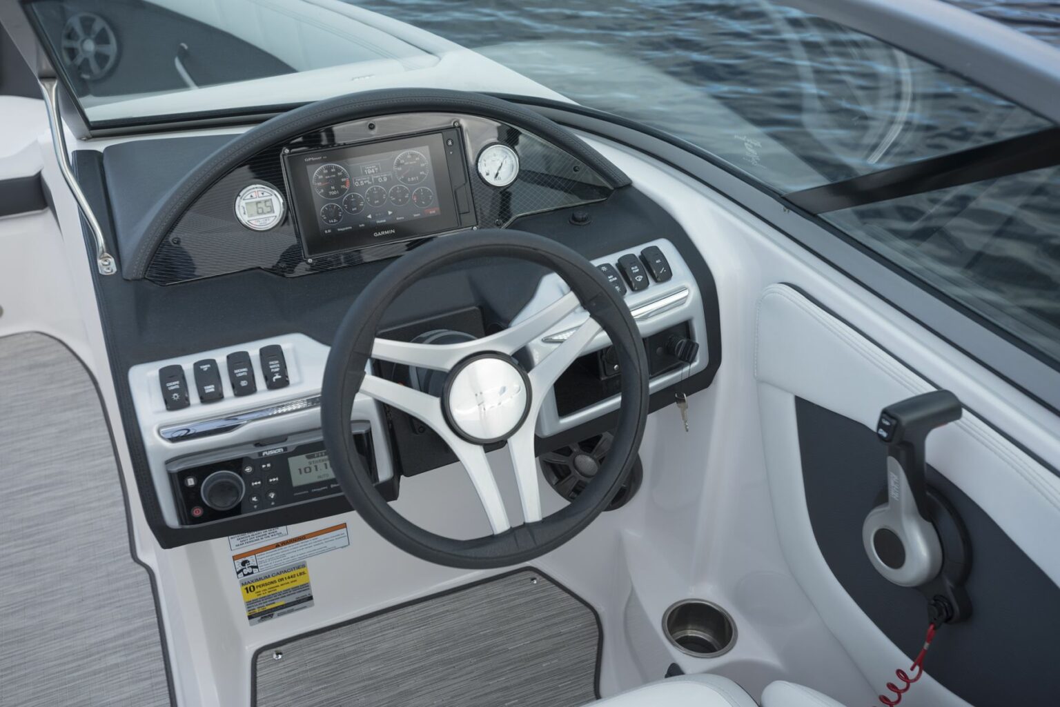 License-free image - The cockpit of a modern boat, featuring a steering wheel, dashboard with various controls, touchscreen display, switches, and instrumentation. The scene shows the interior from the driver&#039;s perspective with a view of the water outside. A capacity plate and certificate of compliance.