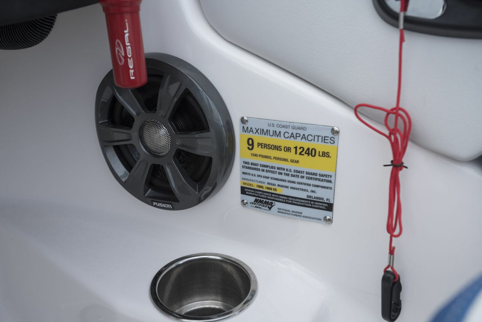 Royalty-free image - This image shows a close-up view of a boat&#039;s interior. Visible are a speaker, a fire extinguisher marked &quot;RELEASE,&quot; a cup holder, and a sign indicating the maximum capacity as 9 persons or 1240 lbs. A safety cord is also attached nearby. A capacity plate and certificate of compliance.