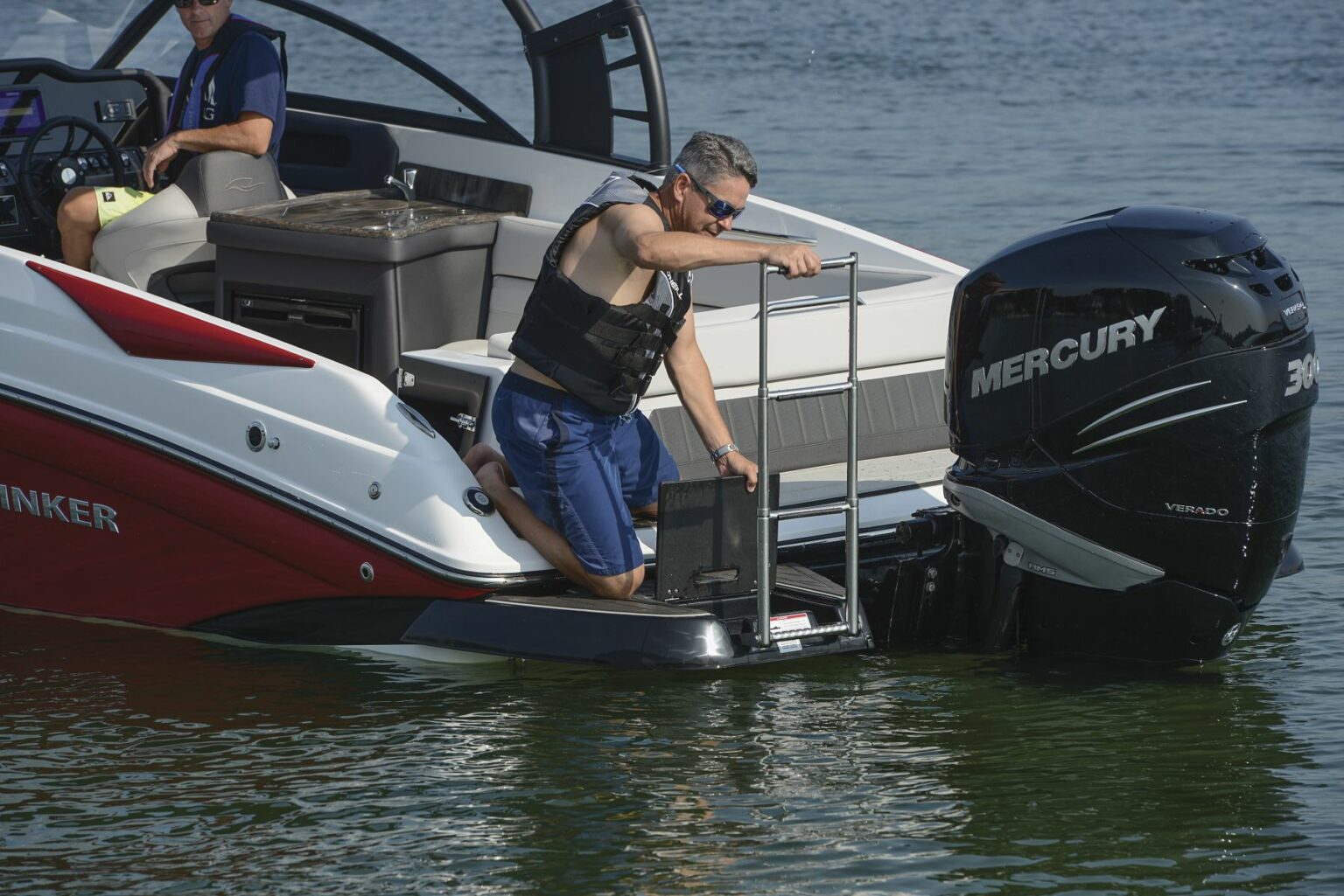 License-free image - A person in a properly fitted USCG approved life jacket is climbing a ladder onto a red and white boat from the water. Another person is seated inside the boat, wearing sunglasses and a blue shirt. A large black Mercury outboard motor is at the back of the boat.