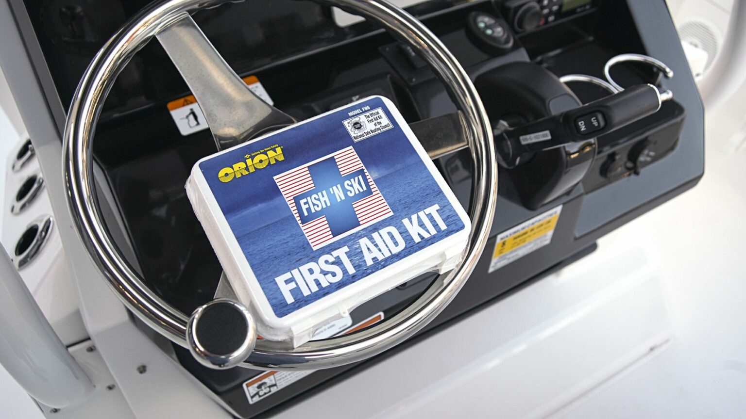 Royalty-free image - A close-up of a boat&#039;s steering wheel and control panel. Attached to the wheel is a first aid kit labeled &quot;Orion Fish &#039;N Ski First Aid Kit.&quot; The kit is sealed in a clear plastic case and positioned in front of the wheel for easy accessibility. A first aid kit, essential equipment on vessels of any size.