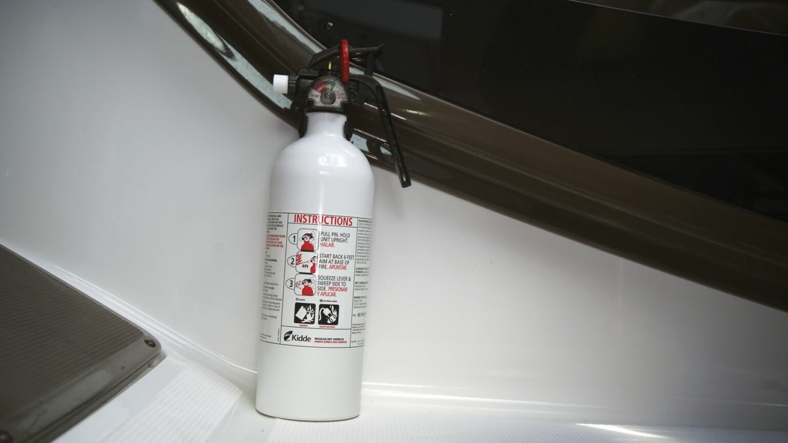 License-free image - A white fire extinguisher with a red and black nozzle is mounted against a white wall. It has a label with instructions for use printed in red and black text, including a graphic of a person using the extinguisher. A mounted fire extinguisher, easily accessible in the event of an emergency.