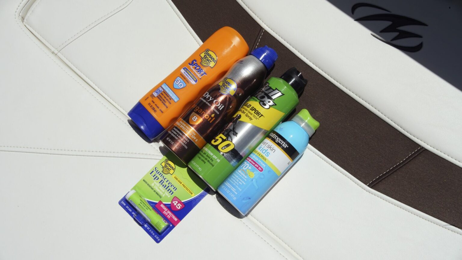 License-free image - Five sunscreen products are lined up on a white surface. The products include CopperTone Sport SPF 30, Banana Boat UltraMist SPF 50, NO-AD SPF 50, Neutrogena Ultra Sheer Body Mist SPF 100+, and Banana Boat Ultra Defense SPF 50. Sunscreen is essential gear on any sized vessel.