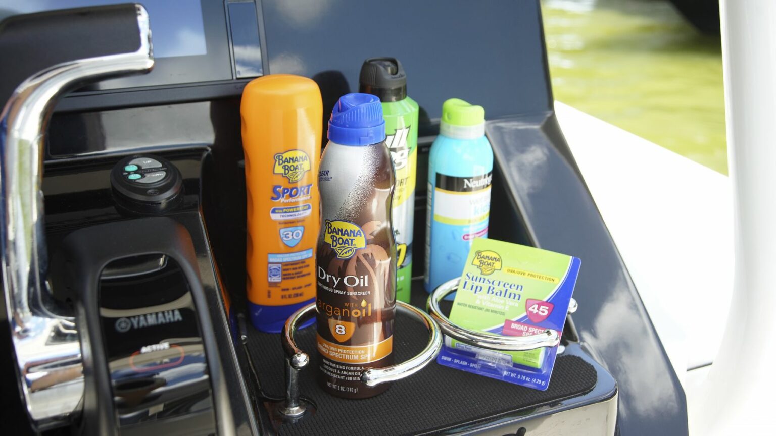 License-free image - A close-up of various sunscreen and skincare products on a boat&#039;s console. Visible brands include Banana Boat and Neutrogena. Items range from SPF 30 - 50, with products like dry oil, sport lotion, spray sunscreen, and lip balm sunscreen. Sunscreen is essential gear on any sized vessel.