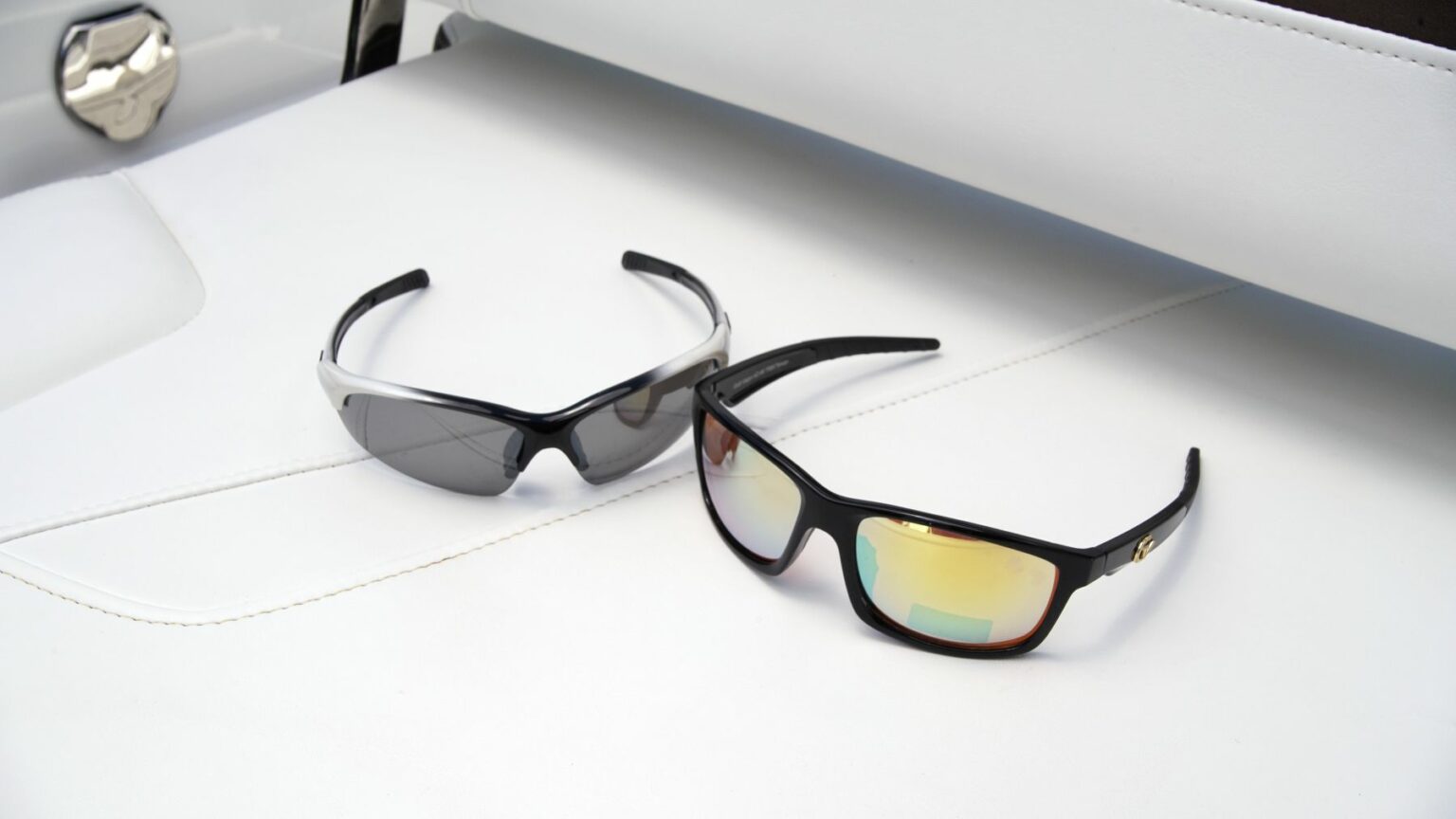 License-free image - Two pairs of sunglasses rest on a white surface. The pair on the left has a sleek design with dark lenses and black-and-white frames, while the pair on the right features reflective yellow-tinted lenses with black frames. Sunglasses are essential gear on any sized vessel.