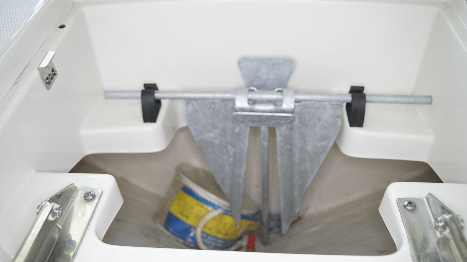 License-free image - A boat&#039;s anchor is securely stowed in an anchor locker. The anchor is fixed in place by a metal bar, and there&#039;s a yellow, blue, and white bucket stored in the locker as well. The compartment is clean and appears well-maintained. A fluke, danforth, or lightweight anchor.