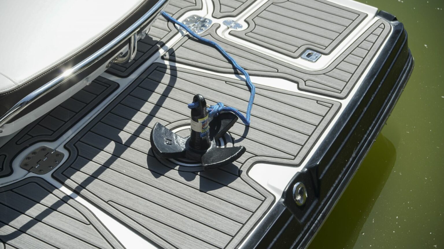 License-free image - A boat&#039;s swim platform with non-slip decking material is shown next to greenish water. A black suction anchor with a blue rope attached is placed on the platform, indicating that it might be used for securing water sports equipment or docking. A pronged mushroom anchor, primarily used on rivers.