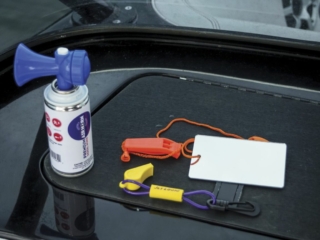License-free image - A blue air horn, a small orange whistle, a white card, and brightly colored key floats lie on a black surface. The items are used for safety and identification during boating activities. Sound producing devices used to attract attention while boating.