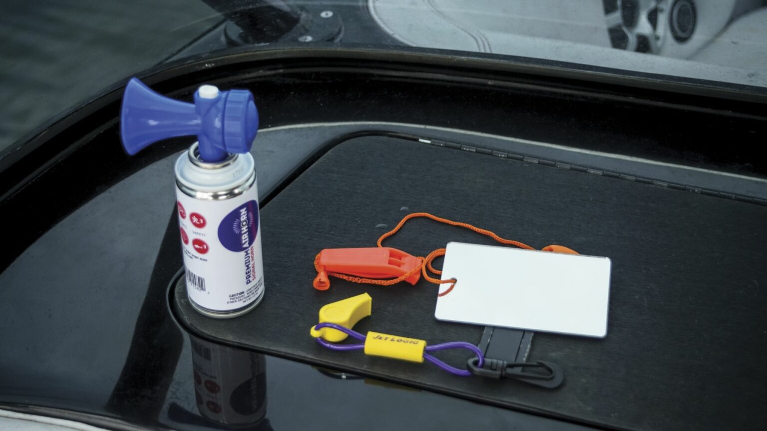 License-free image - A blue air horn, a small orange whistle, a white card, and brightly colored key floats lie on a black surface. The items are used for safety and identification during boating activities. Sound producing devices used to attract attention while boating.