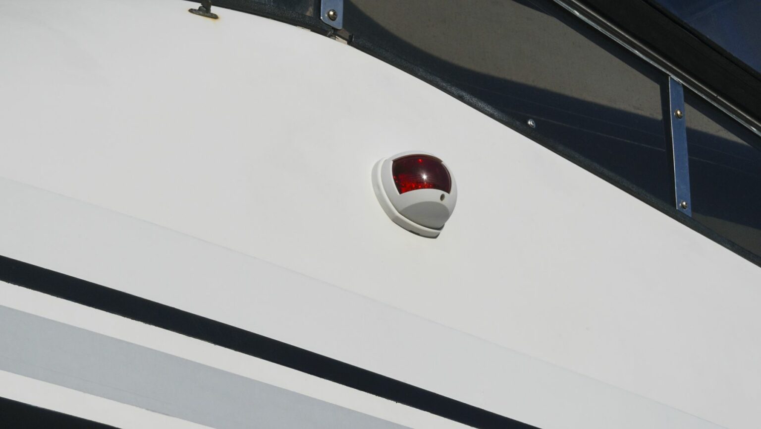 License-free image A close-up of a white boat&#039;s side, featuring a rounded red and white light fixture mounted on the exterior. The boat has clean lines and a modern design, with a part of a window frame visible at the top of the image.