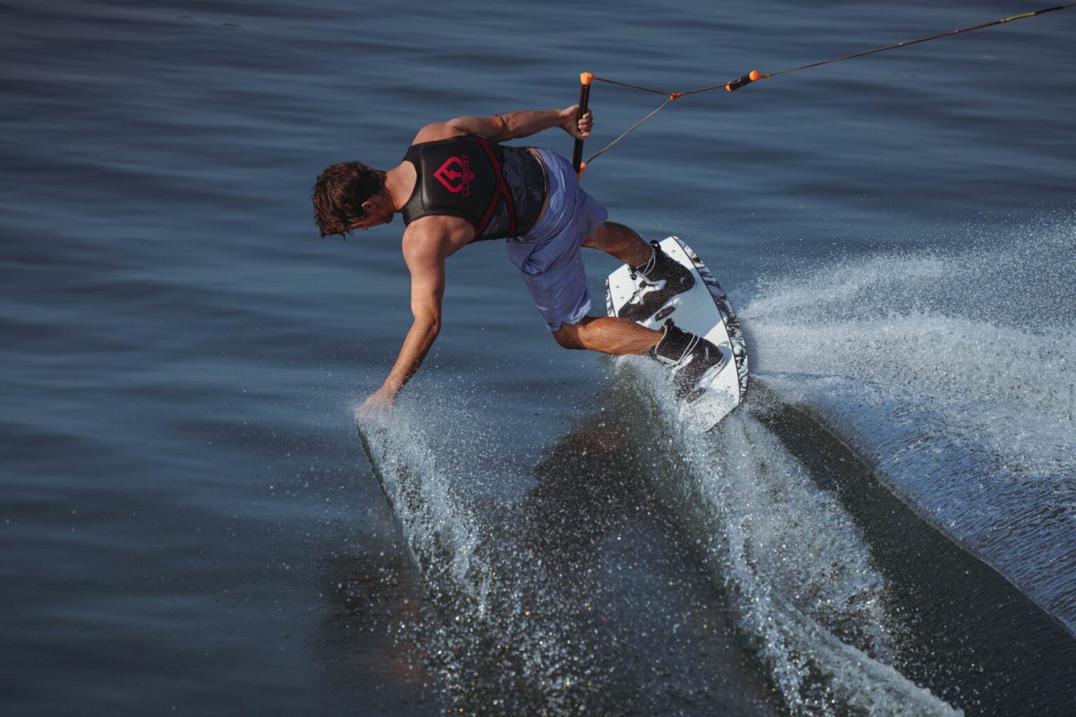 License-free image - A person wearing a life vest and shorts is wakeboarding on a body of water. The individual is balancing on a surfboard-like equipment, creating splashes as they perform a dynamic maneuver. The water surface is calm, with ripples caused by the wakeboarding action.