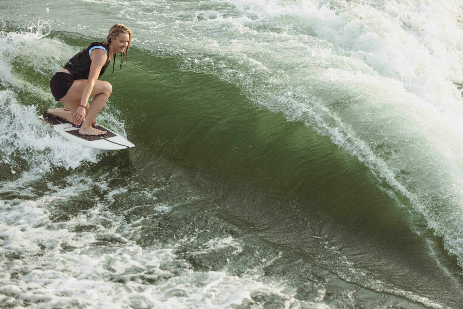 License-free image - A person with braided hair is surfing on a large wave in the ocean. They are wearing a sleeveless wetsuit and skillfully maneuvering the surfboard, creating a dynamic scene with splashing water all around.